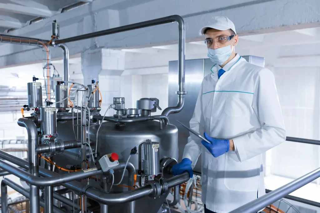 Un técnico de laboratorio con bata blanca, máscara y guantes azules manipula un sistema de filtración al vacío en una planta química
