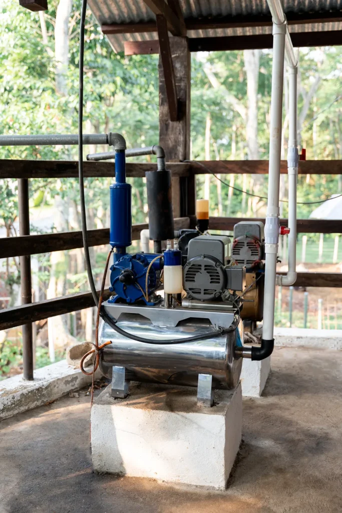 Primer plano de un sistema de bombeo de agua con filtración al vacío montado en bloques de concreto con tuberías y un motor eléctrico.
