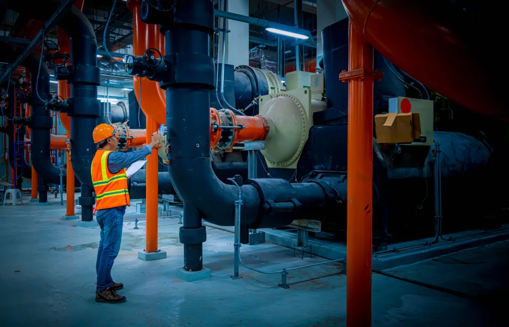 Ingeniero de mantenimiento industrial inspeccionando sistemas de climatización con tuberías y equipos complejos.