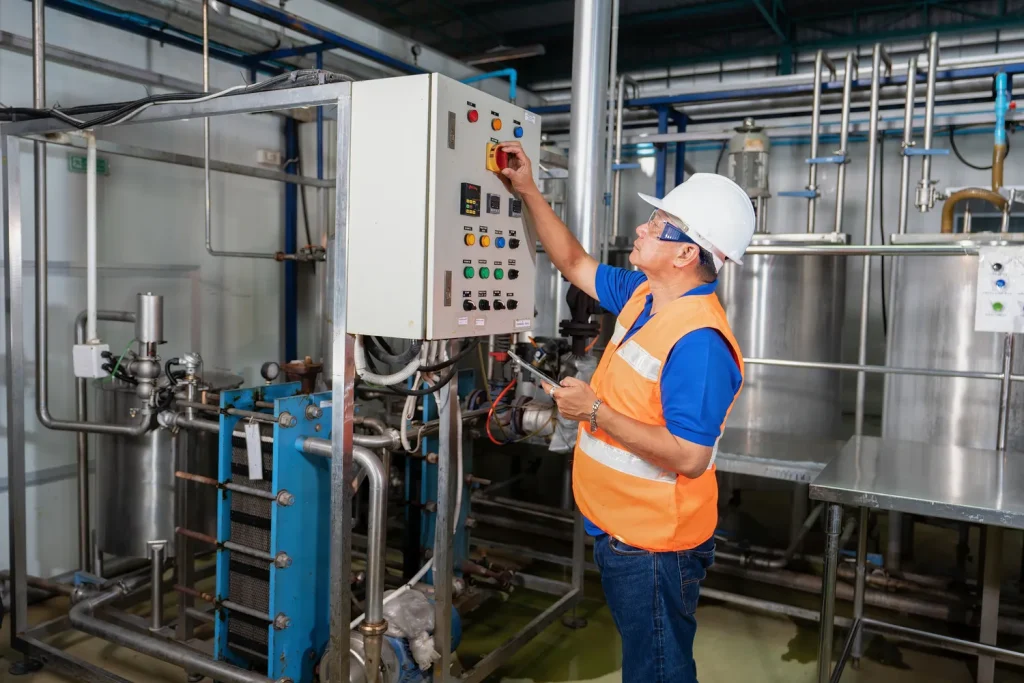 Técnico de mantenimiento industrial operando un panel de control con interruptores y luces en una fábrica.