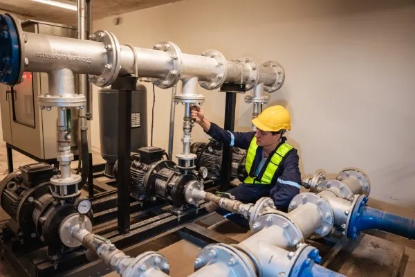 Ingeniero con casco amarillo realiza mantenimiento preventivo en una red de tuberías y bombas de agua industriales.